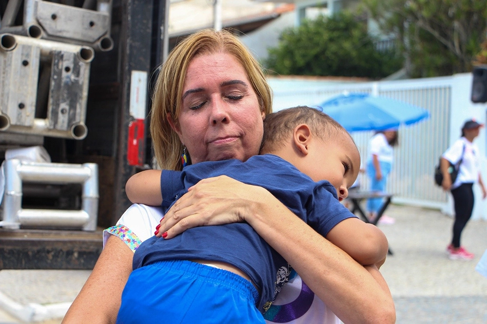 Lucia abraçando uma criança que está apoiando a cabeça em seu ombro.