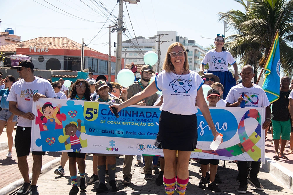 Lucia posando na frente da faixa da 5ª caminhada do dia mundial da concientização do autismo.
